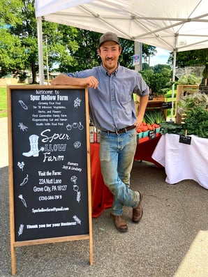 Jeff Spur Hollow Farm standing in front of booth at farmers market 