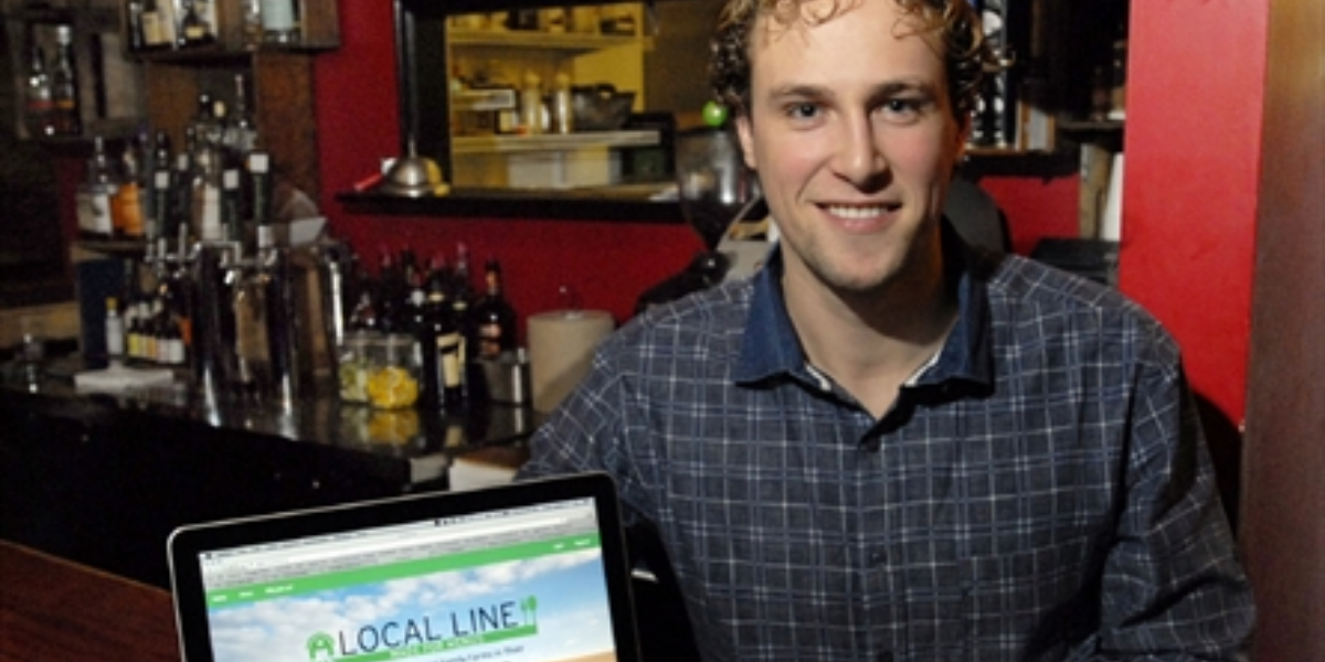 Cole Jones, founder of Local Line, smiling next to a computer with his platform visible on the screen