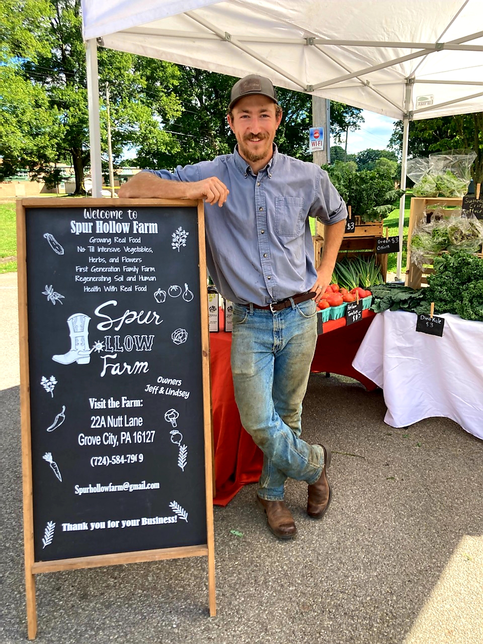Man standing in booth at farmers market with fresh produce 